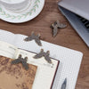A vintage butterfly metal book clip rests on a notebook next to a laptop and a teacup.
