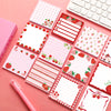 A set of pink and red strawberry-shaped self-stick memo notes and a white keyboard are displayed on a pink background.