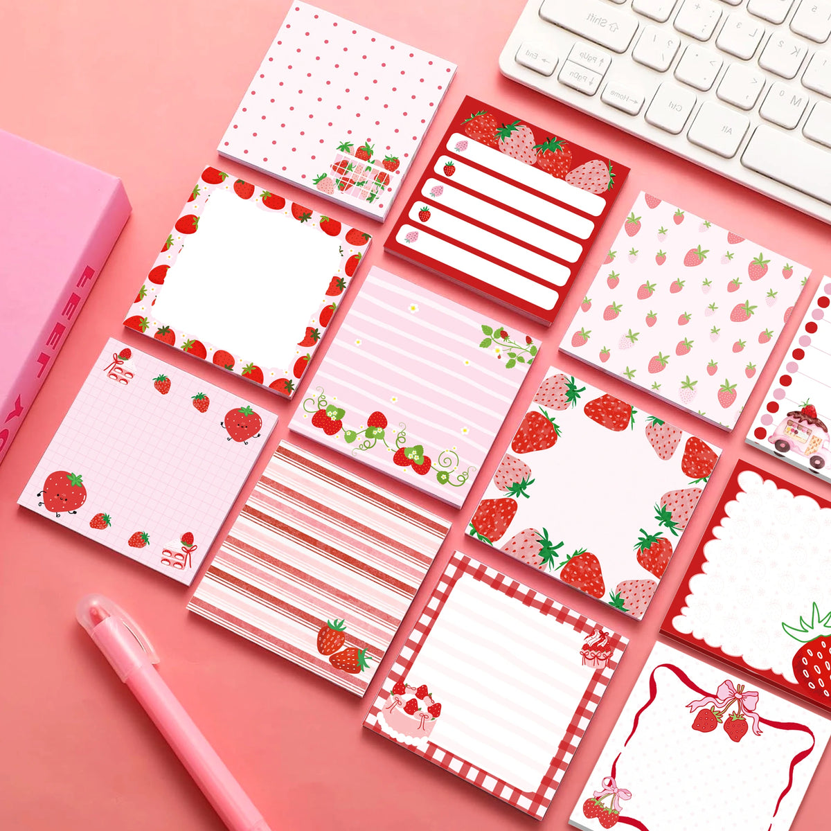 A set of pink and red strawberry-shaped self-stick memo notes and a white keyboard are displayed on a pink background.