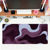 A dark purple and white abstract wave mouse pad placed on a wooden desk next to a computer setup.