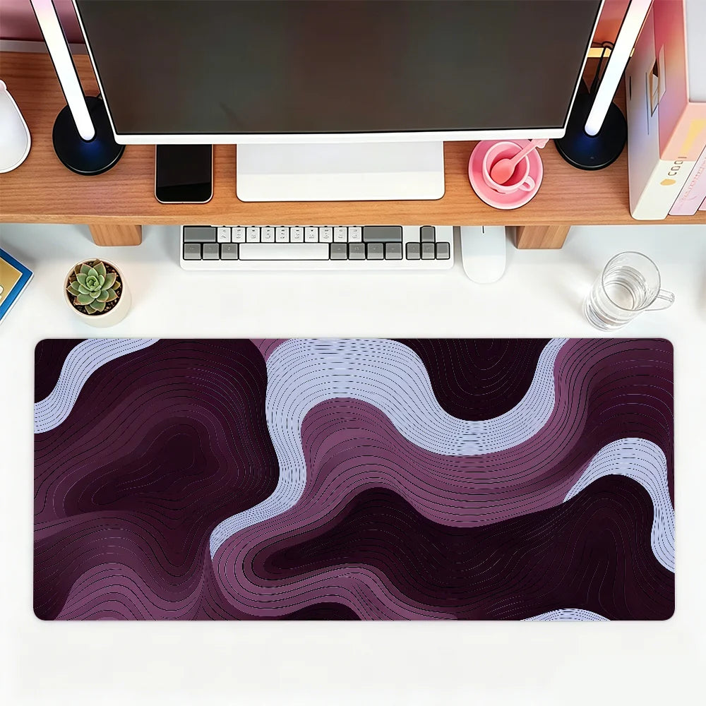 A dark purple and white abstract wave mouse pad placed on a wooden desk with a computer setup.