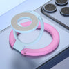 A pink and white magnetic ring grip with a foldable kickstand shown on a gray surface.