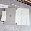Un iPad plateado con una funda blanca protectora y un lápiz óptico sobre una superficie de hormigón gris.