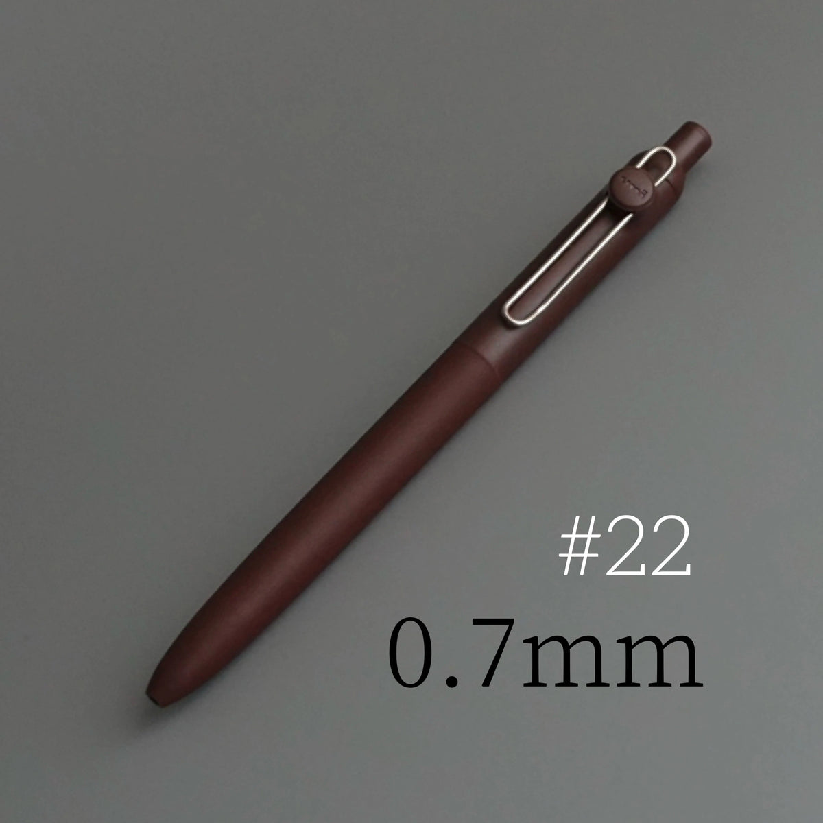 A brown precision gel pen with a silver-colored tip is shown diagonally on a gray background.