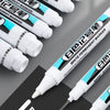 A close-up view of several white permanent paint marker pens with various tips and sizes displayed on a dark surface.