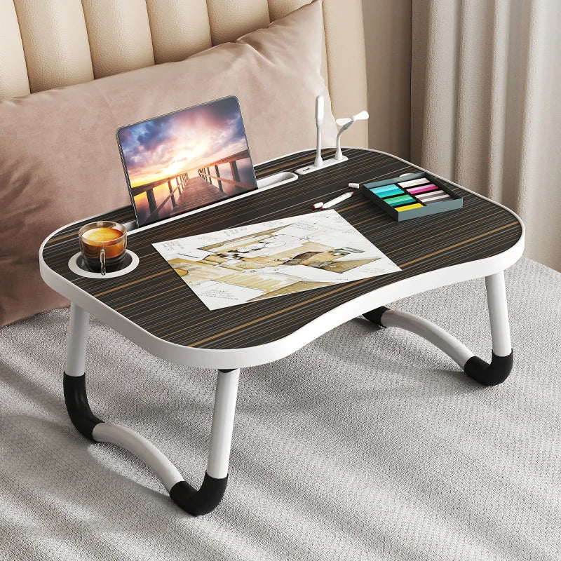 A multi-functional laptop desk organizer tray with a wooden surface holding a laptop, a cup, and art supplies.
