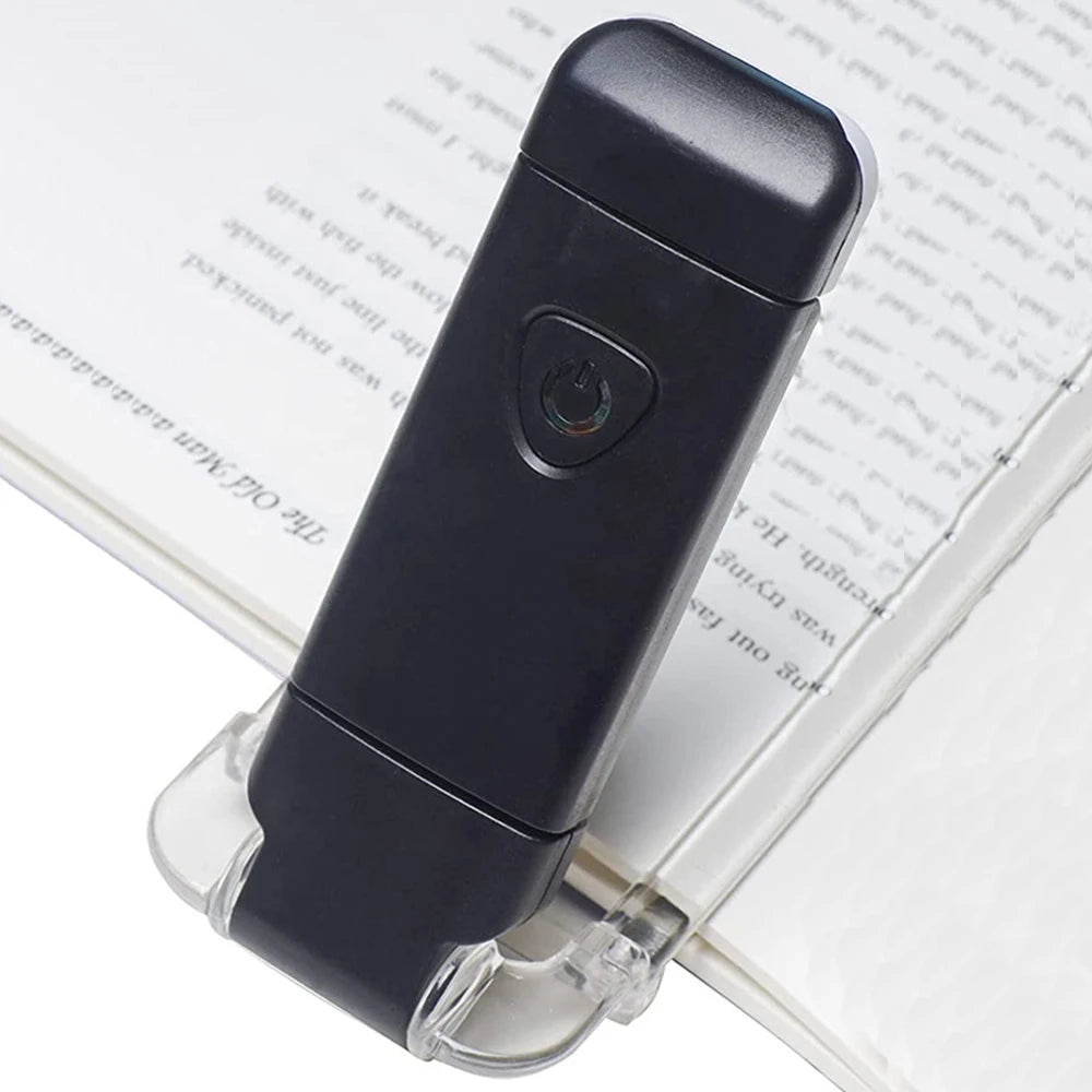 A black USB rechargeable LED book reading light is shown resting on a white page.