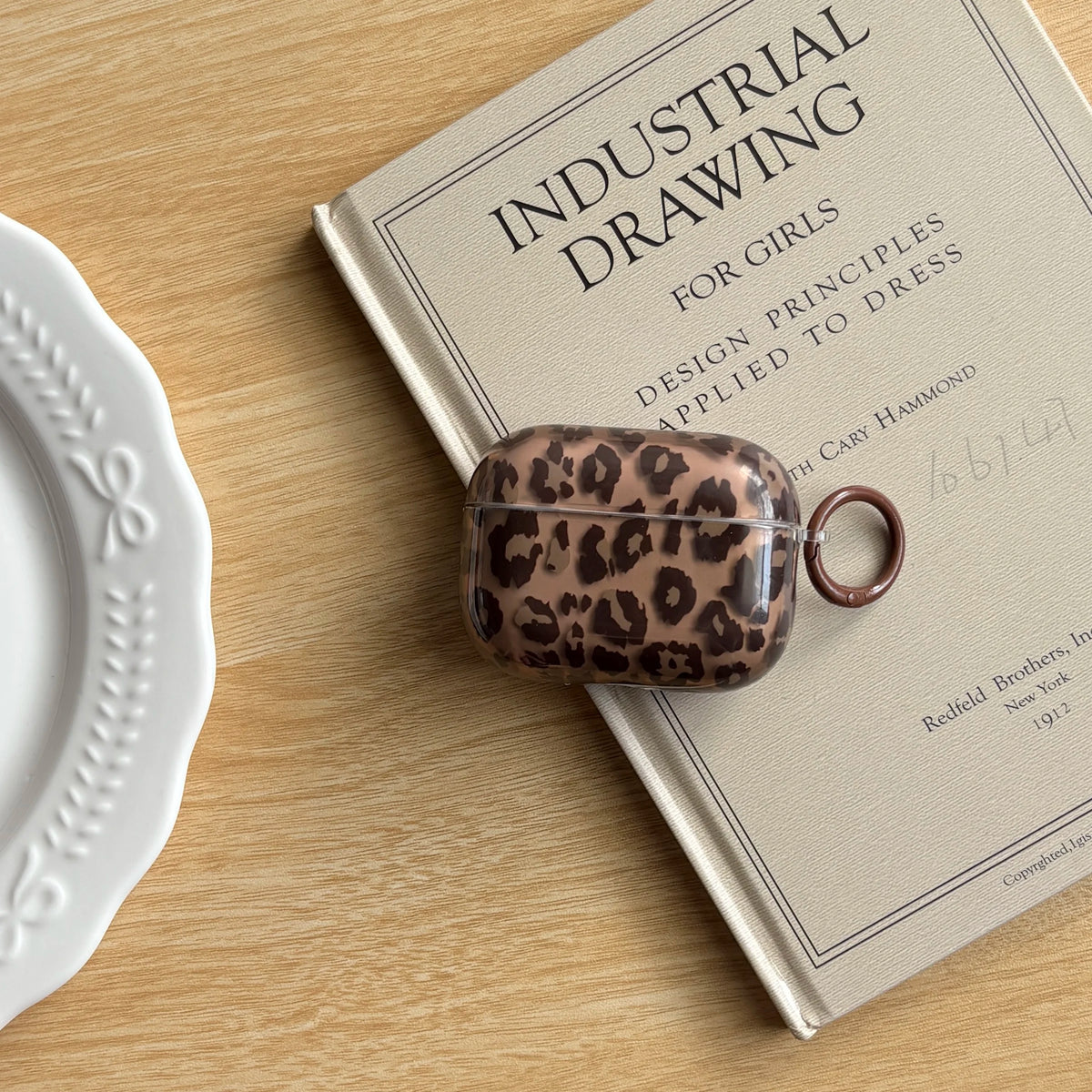 A brown leopard print earphone case cover resting on a page of an industrial drawing book.