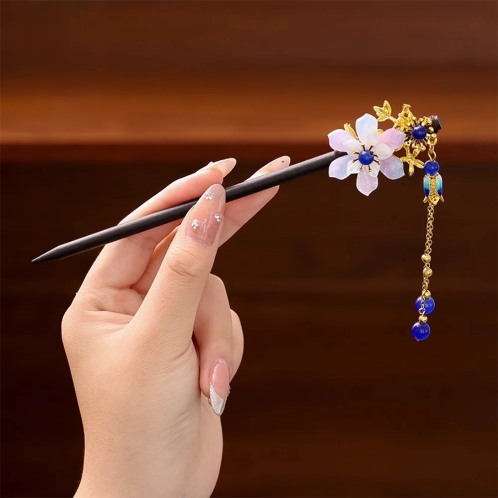 Une main tient un pinceau noir avec des accessoires pour cheveux floraux dorés, featuring des fleurs violettes et bleues et d