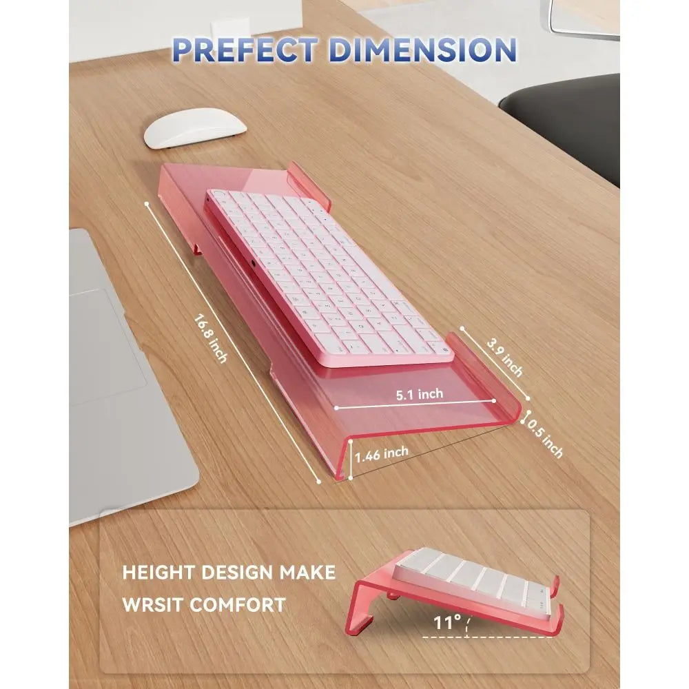 Pink acrylic keyboard riser stand with ergonomic wrist rest shown on a wooden desk surface.