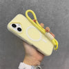 A hand holds a yellow phone case with a white circular design and a yellow lanyard against a gray background.