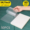 A hand holds a clear thermal laminating pouch, showing its size and thickness on a grid background.