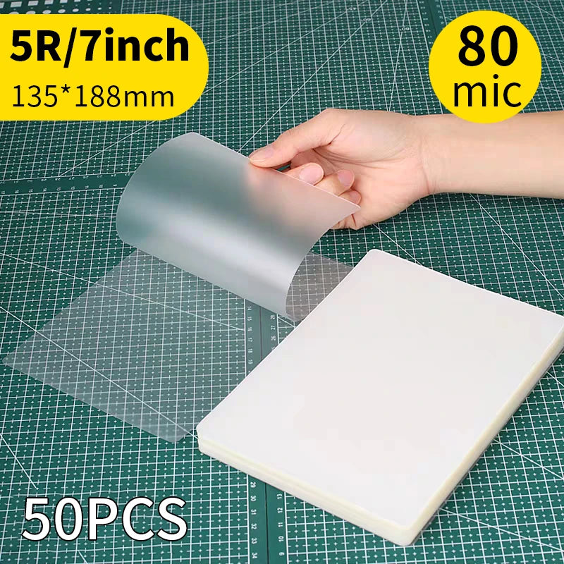 A hand holds a clear thermal laminating pouch, showing its size and thickness on a grid background.