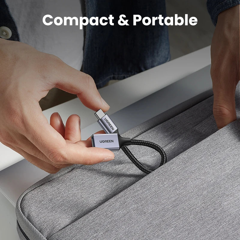 A hand holds a compact USB-C to USB 3.0 OTG adapter with a black cable against a gray fabric background.