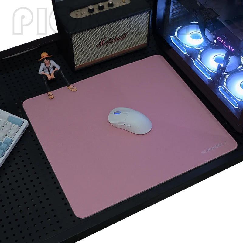 A pink professional gaming mouse pad is placed on a black desk mat next to a mouse and a small figure.