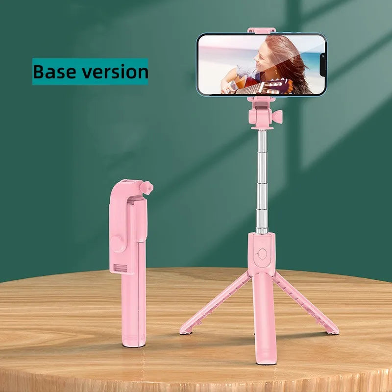 Pink selfie stick tripod with fill light and wireless remote positioned on a wooden table.