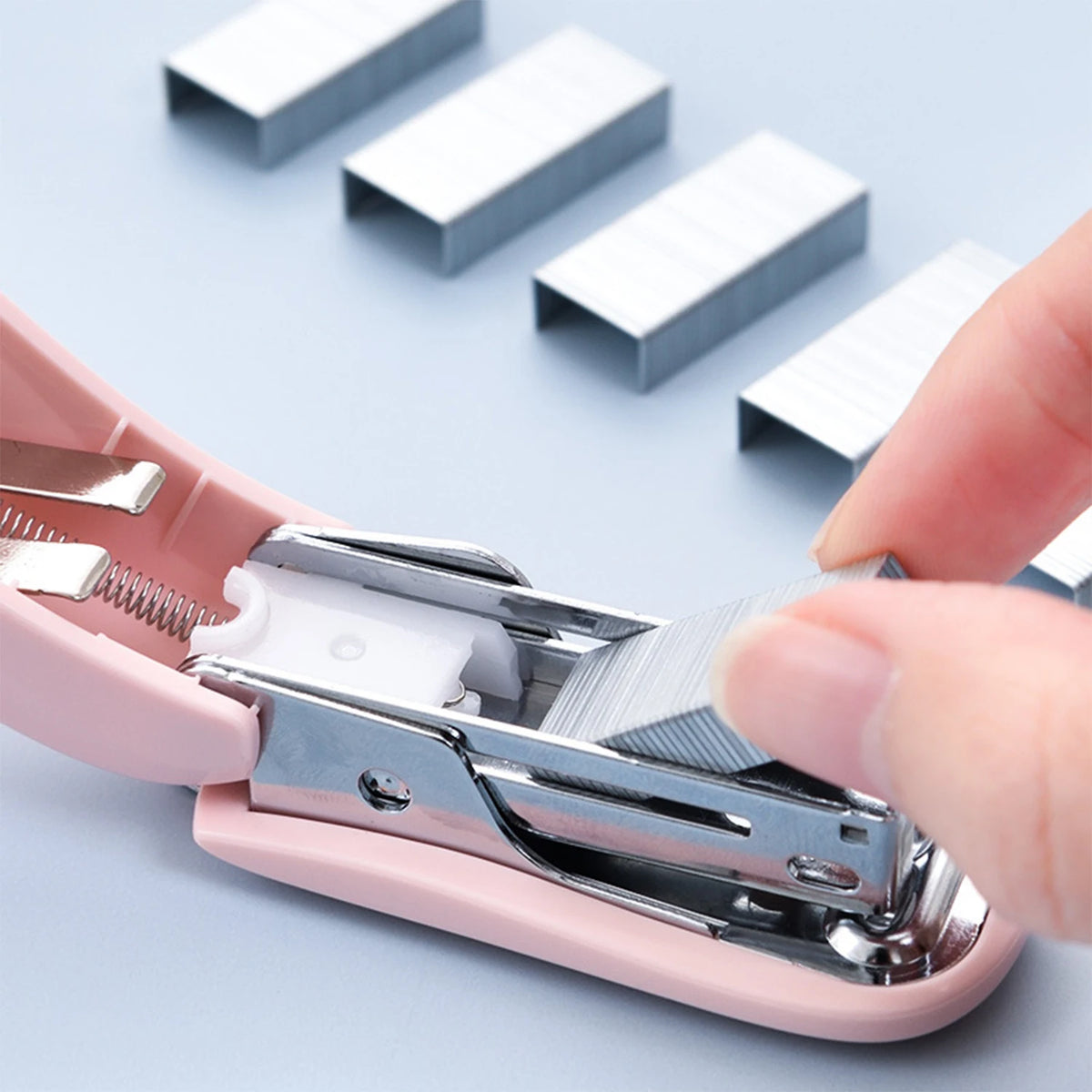 A hand is operating a pink compact mini stapler kit, demonstrating the use of staples.