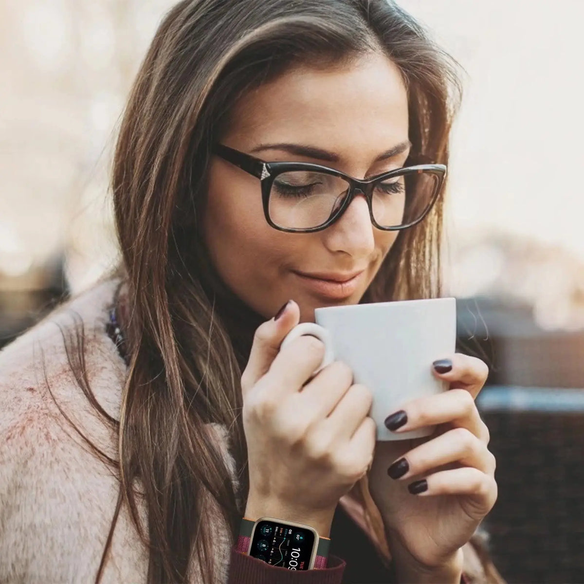 A woman wearing black glasses holds a white mug while looking down, with an adjustable sport hook and loop watch strap visibl