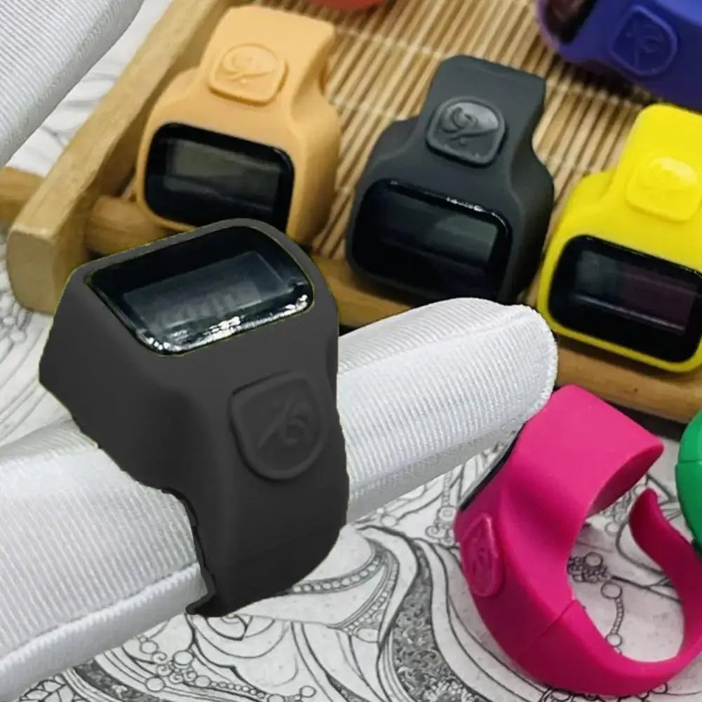 A black thumb tally counter device is shown resting on a white foam grip, surrounded by other yellow and black digital counte