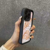 A hand holds a black phone case with a croissant newspaper pattern design for an iPhone.