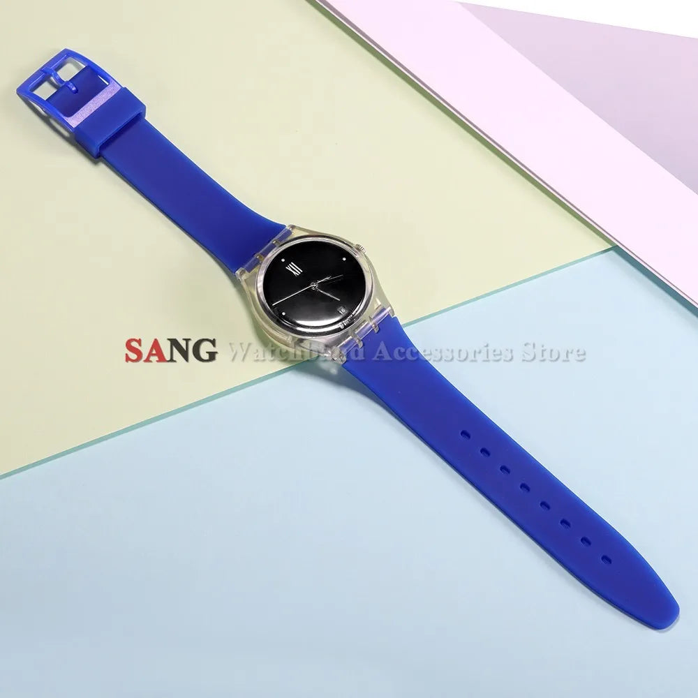 A blue silicone watch strap with a silver watch and replacement tools is displayed on a light background.