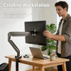 A man is using a clean cable layout desk edge clamp monitor arm to position a laptop on a wooden desk.