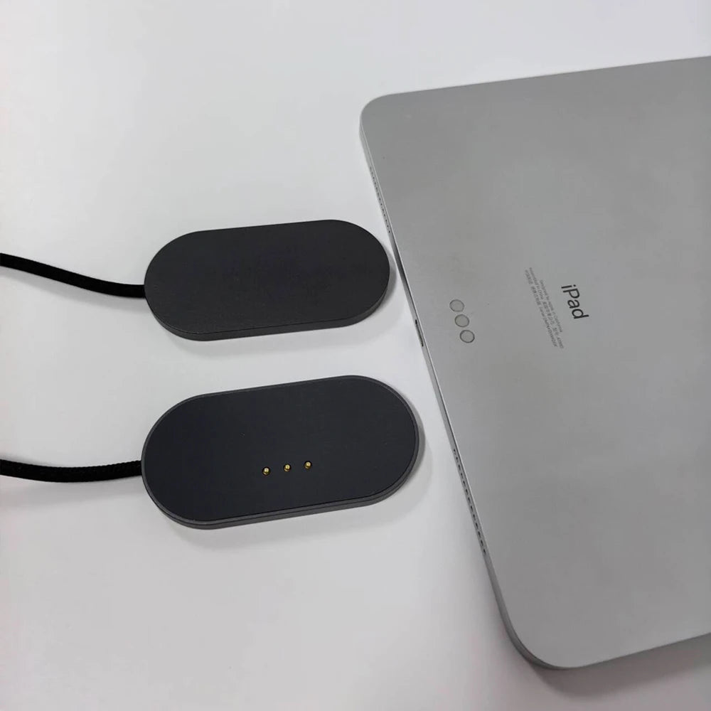 A silver iPad is shown next to its magnetic wireless charging adapter, which has three charging pins.