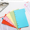 A stack of colorful A6 budget planner pages and a blue binder with envelope pockets for separation.