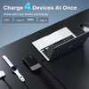 A portable power bank is shown charging four devices simultaneously, including a laptop and a smartwatch.