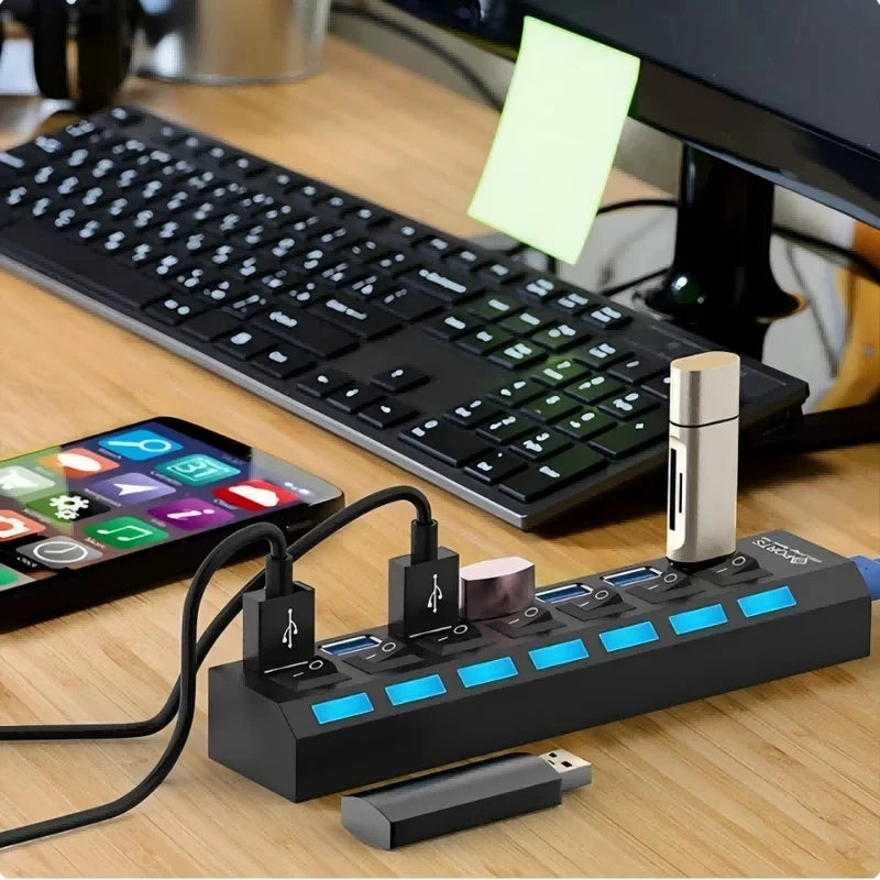Schwarzer 7-Port-USB 2.0-Hub mit Kabeln und einem Adapter auf einem Holzschreibtisch.
