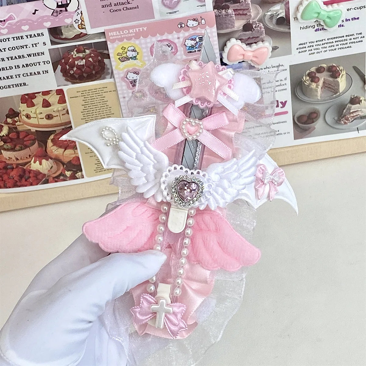 A hand holds an intricate pink and white angel wing art knife cutter with a decorative bow and pearl accents.