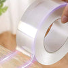 Hand applying a roll of clear adhesive tape to a wooden surface, showing the tape's glow.