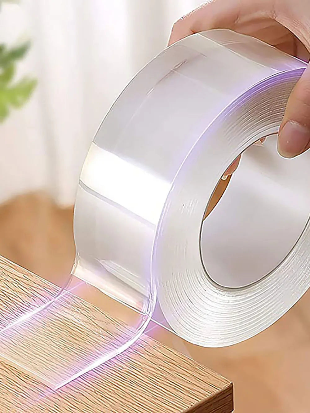 Hand applying a roll of clear adhesive tape to a wooden surface, showing the tape's glow.