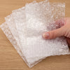 A hand is holding a sheet of transparent bubble wrap padded shipping bags on a wooden surface.