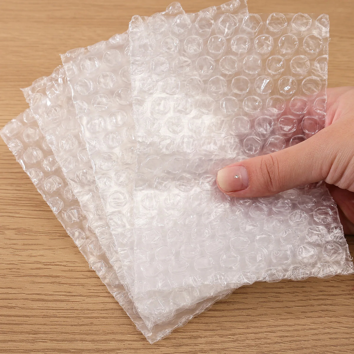 A hand is holding a sheet of transparent bubble wrap padded shipping bags on a wooden surface.