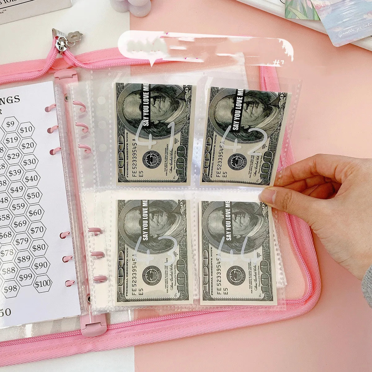 A pink envelope binder set containing stacks of US dollar bills and paper currency.