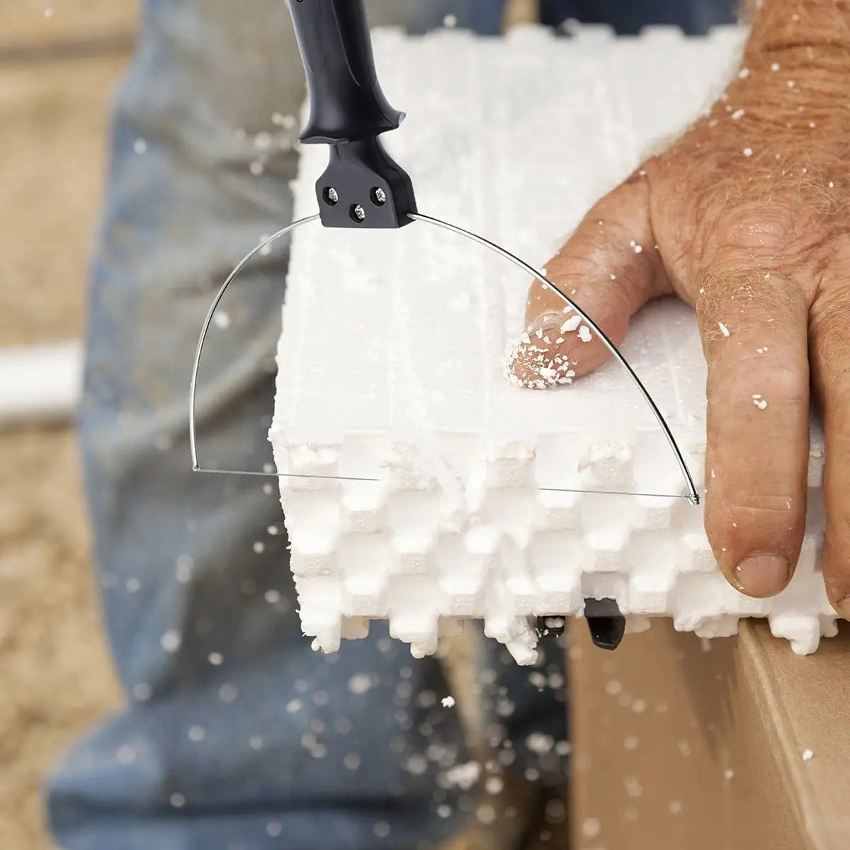 A hand uses an electric foam cutting tool to cut a piece of white insulation foam.