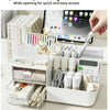 A white multifunctional desk organizer with clear storage drawers and various office supplies is shown on a light surface.
