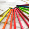 A collection of metallic fluorescent colored pencils in various shades of pink, orange, yellow, and green laid out on a white