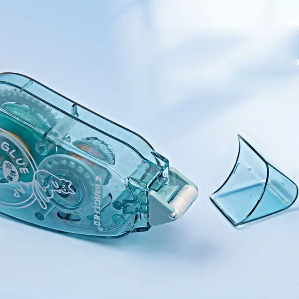 A clear plastic double-sided adhesive tape dispenser and a piece of the tape on a light blue background.