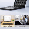 A black foldable Bluetooth keyboard is shown in two contexts: a home office setup and during a business trip.
