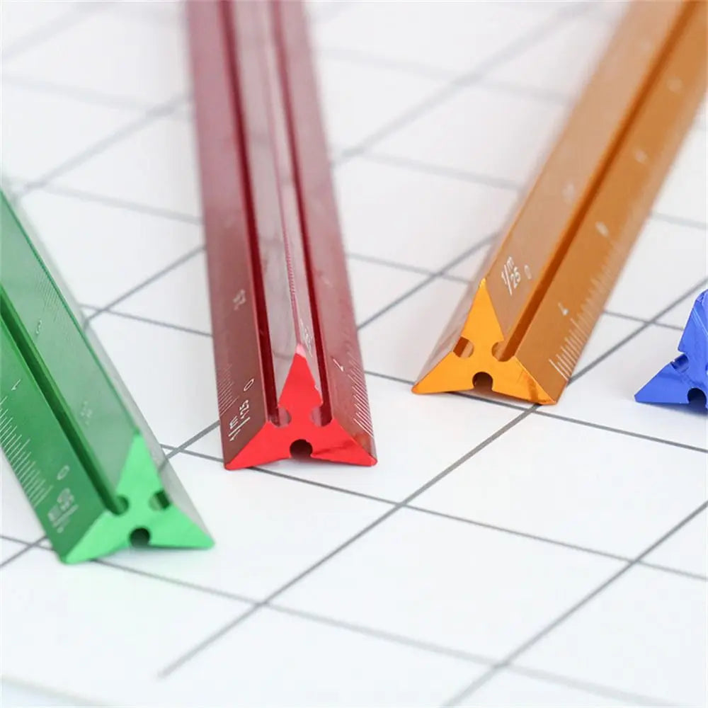 A set of aluminum triangular scale rulers in red, orange, and green lying on a white grid background.