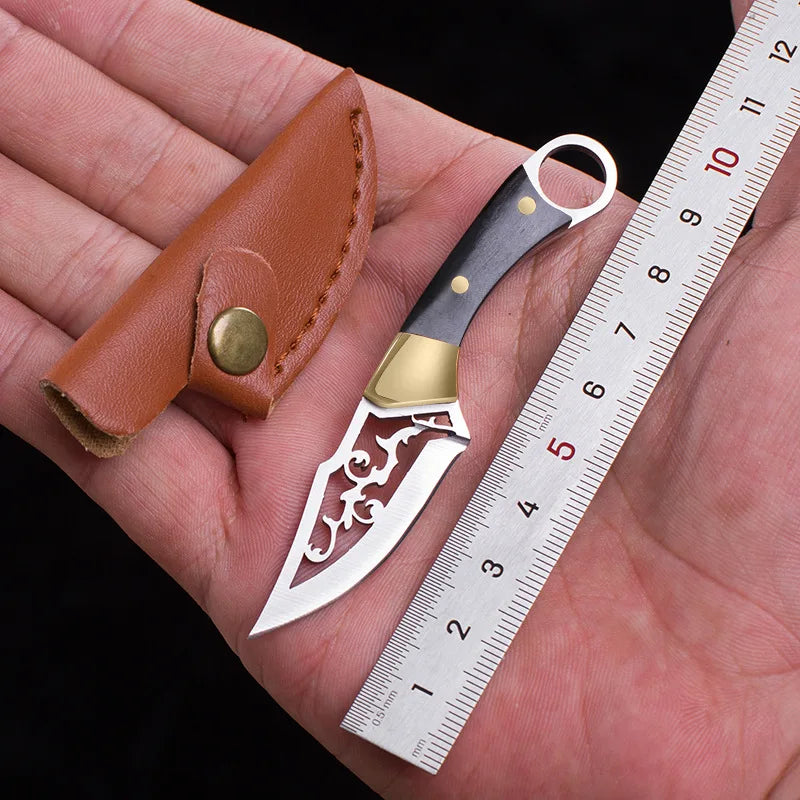 A compact fixed blade knife with a silver blade and gold accents is shown next to a ruler on a hand.