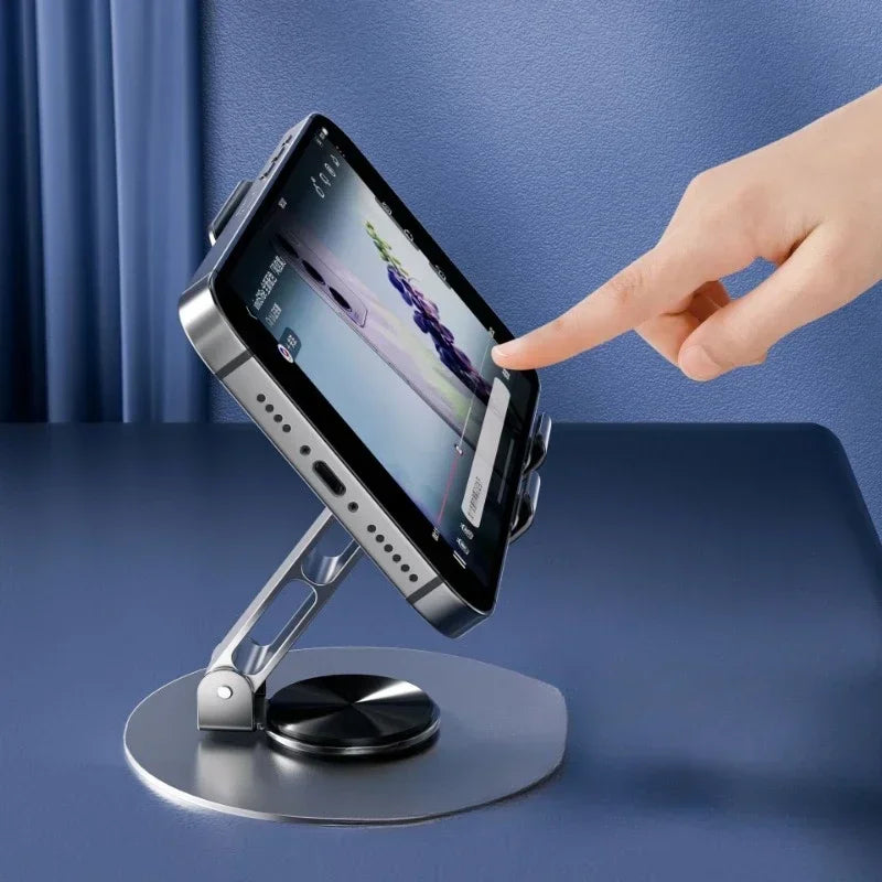A hand is rotating a mobile phone holder device that supports a smartphone for viewing.