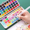 An open watercolor paint palette showing various solid colored paints and a hand applying paint.