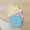 Ein Stapel bunter quadratischer selbstklebender Notizzettel in Pastelltönen, darunter rosa, grün, gelb und blau.