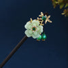 Accessoires pour cheveux floraux dorés avec des fleurs vert clair et des perles vert émeraude sur un bâton en bois foncé.