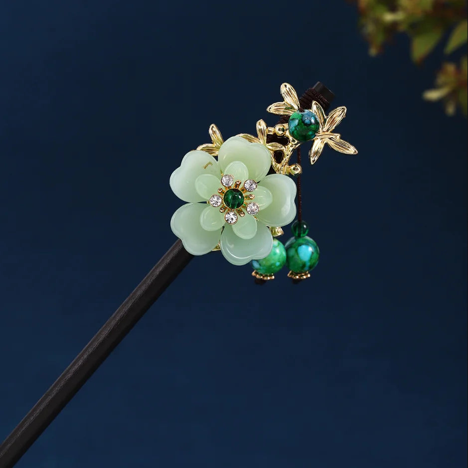 Accessoires pour cheveux floraux dorés avec des fleurs vert clair et des perles vert émeraude sur un bâton en bois foncé.