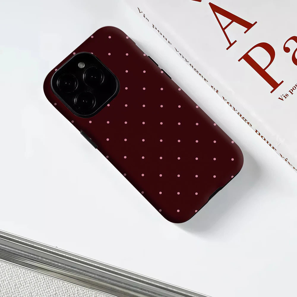 Funda para móvil color granate oscuro con patrón de lunares sutil sobre una superficie blanca.