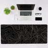A black desk setup featuring a laptop, mouse, keyboard, and a large black and white topographic map mouse pad.